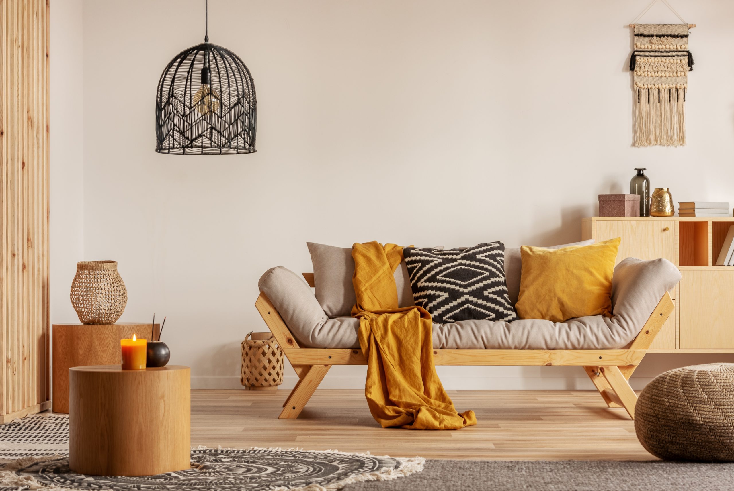 Scandinavian sofa with pillows and dark yellow blanket in bright living room interior with black chandelier